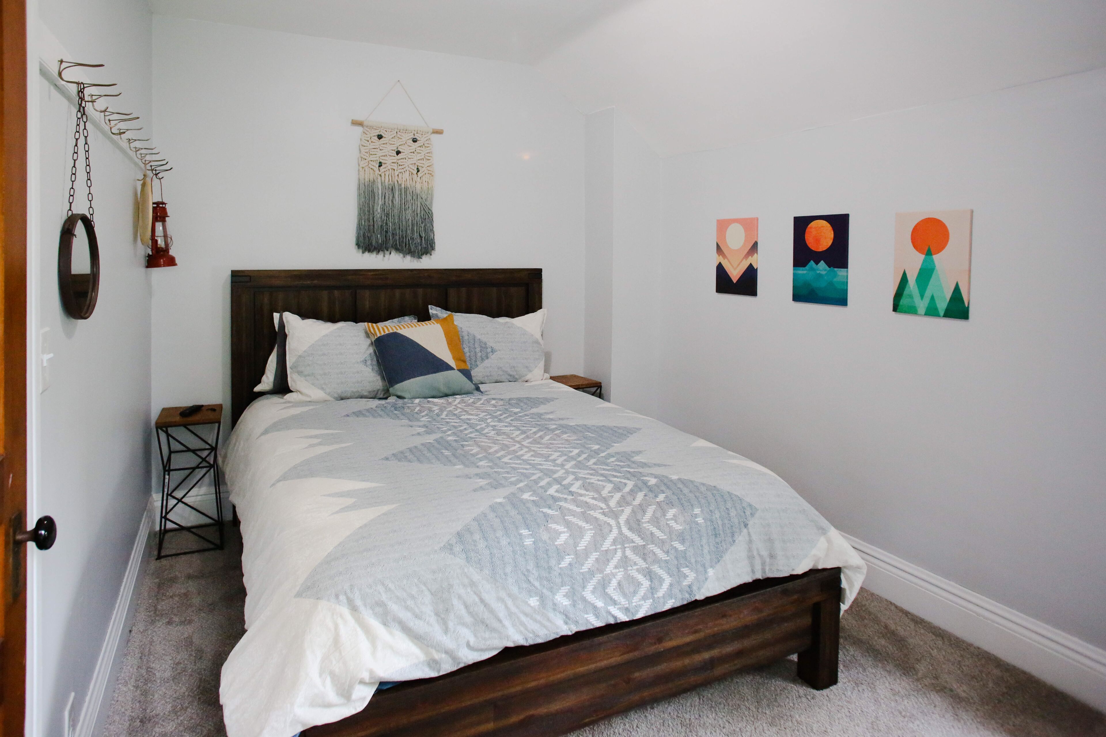 Een net opgemaakt bed met een bedsprei met dessin, een houten hoofdbord en een klein nachtkastje met een lamp.