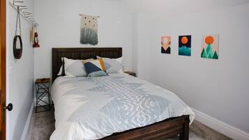 Een net opgemaakt bed met een bedsprei met dessin, een houten hoofdbord en een klein nachtkastje met een lamp.
