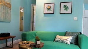 Ein Zimmer mit einem grünen Sofa, einem kleinen Holztisch mit einer Pflanze und zwei gerahmten Pflanzenbildern an der Wand.