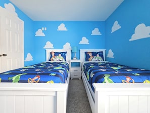 Un dormitorio con dos camas, una puerta blanca y una pared azul decorada con nubes.