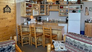 Interior rústico de cabana com zona de jantar de madeira, cozinha com armários de madeira e área de estar acolhedora.