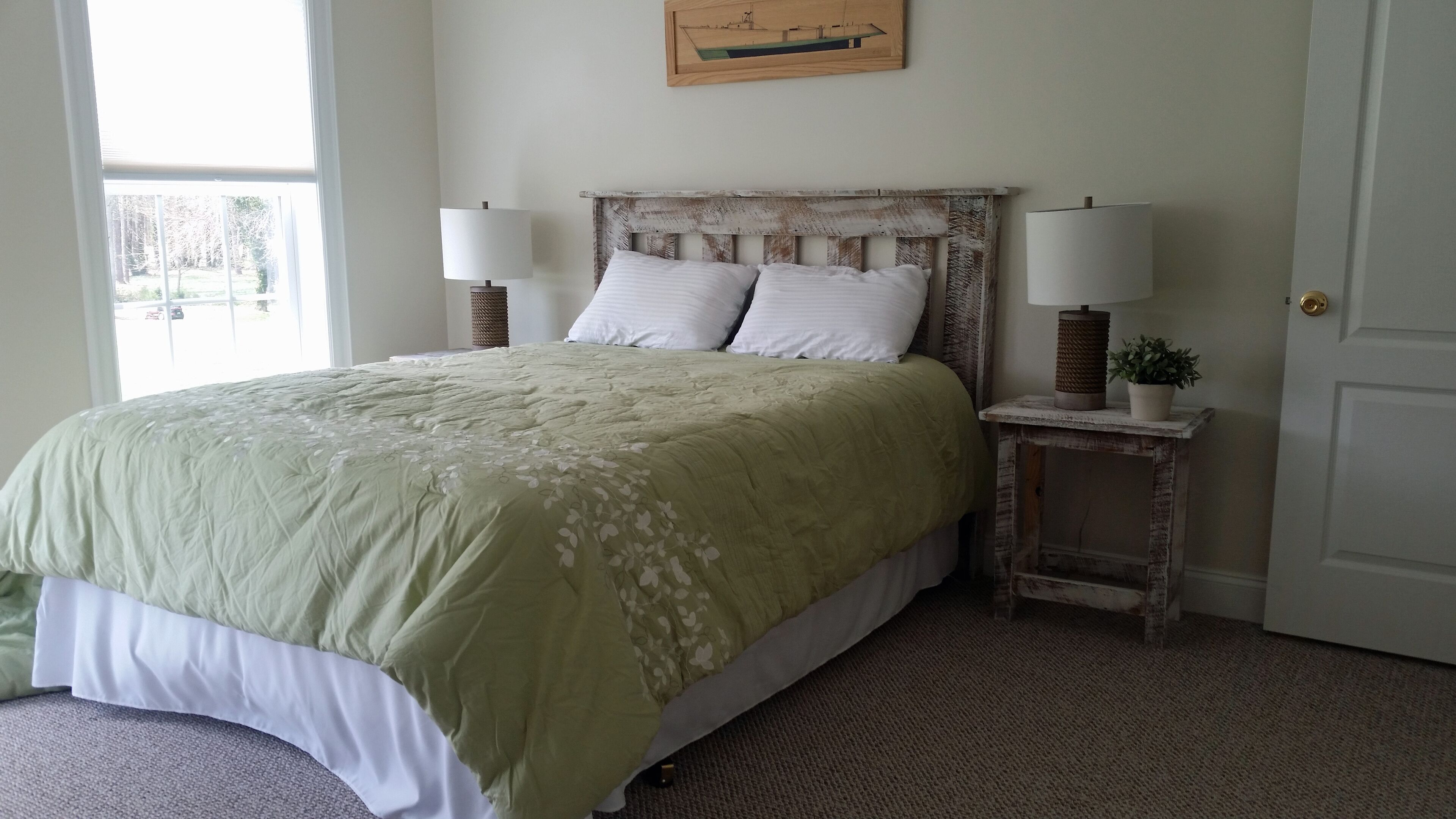 A bedroom with a bed, two bedside lamps, a small table with a plant, and a door.