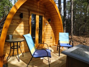 Una cabaña de madera con dos sillas y una mesa en el porche, rodeada de árboles.