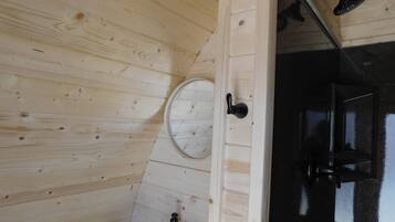 Une salle de bain aux murs lambrissés, avec un lavabo blanc, un miroir rond et une pomme de douche noire.