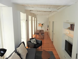 A modern living room with a sofa, a coffee table, and a TV. There is a dining area with a table and chairs in the background.