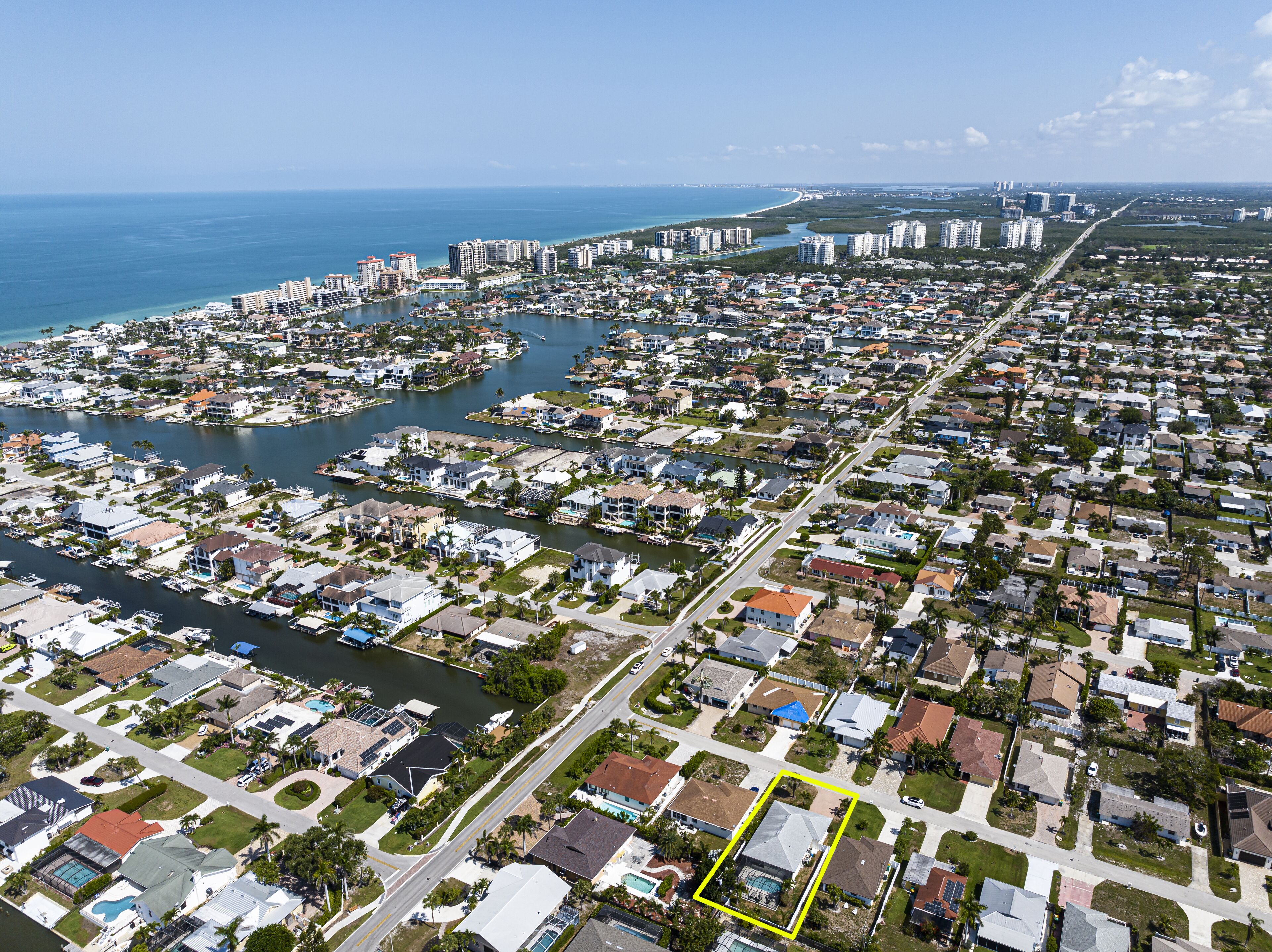 An aerial view of a coastal residential area with a marina, houses, and a beach in the background.