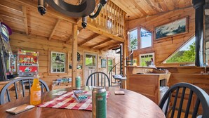 A wooden cabin interior with a dining table, chairs, a kitchen area, and a staircase leading to a loft. - Amazing View! Sauna Gameroom Firepit Spa Room Rustic Spacious Private Retreat  (Banner Elk)