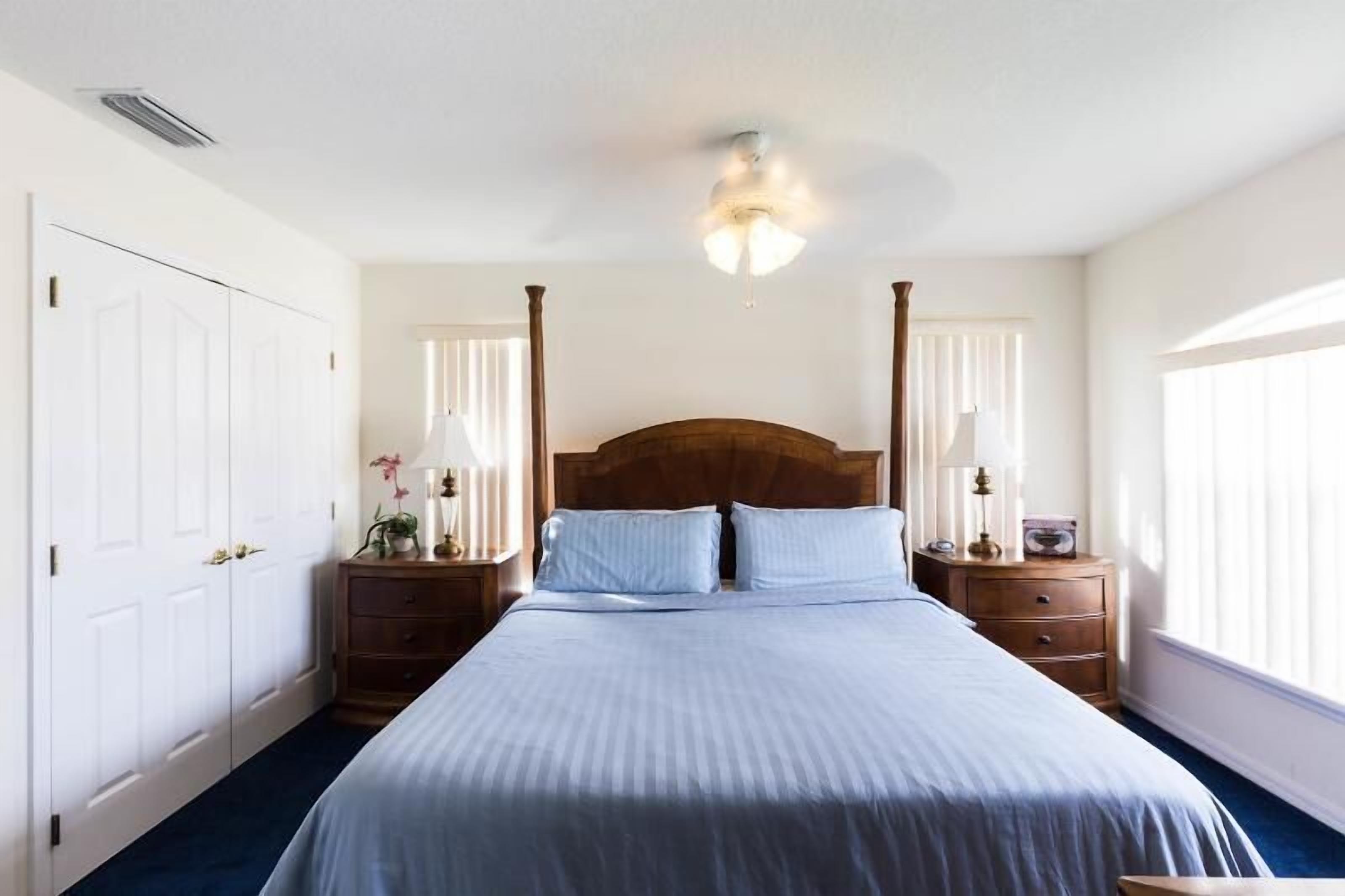 A bedroom with a large bed, two nightstands, a ceiling fan, and a window with blinds.