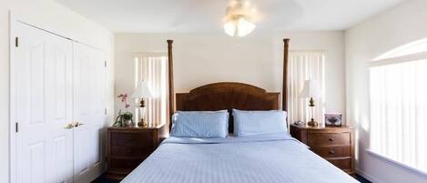 A bedroom with a large bed, two nightstands, a ceiling fan, and a window with blinds.