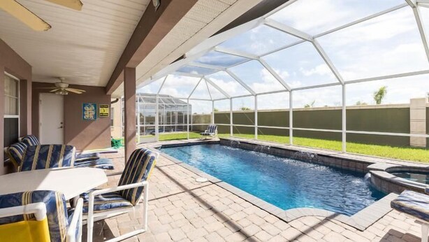 A covered outdoor swimming pool with lounge chairs and a table, surrounded by a glass enclosure.