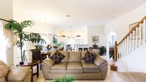 A spacious living room with a beige sofa, a dining table, and a staircase.