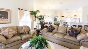 A living room with two beige sofas, a coffee table, and a dining area in the background.