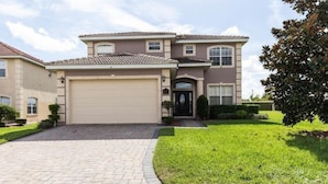A two-story house with a beige garage door, a tiled roof, and a well-maintained lawn.