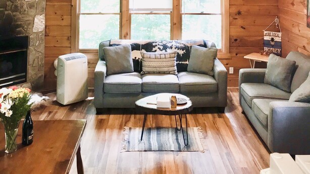 A cozy cabin interior with a stone fireplace, a wooden ceiling, and a sofa with cushions. - ♥♥ Log cabin tree top setting with fire pit!  Sleeping porch. Easy Access (Maggie Valley)