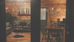 A wooden interior with a sofa, coffee table, and dining area visible through a glass door. - ♥♥ Log cabin tree top setting with fire pit!  Sleeping porch. Easy Access (Maggie Valley)