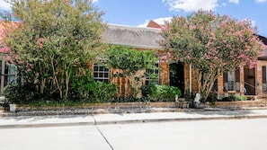 Situated among mature trees and shrubs, this two-story home features a gabled roof and a stone border along the sidewalk.