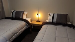 Une chambre d’hôtel avec deux lits simples, une table de chevet avec une lampe et un mur uni.