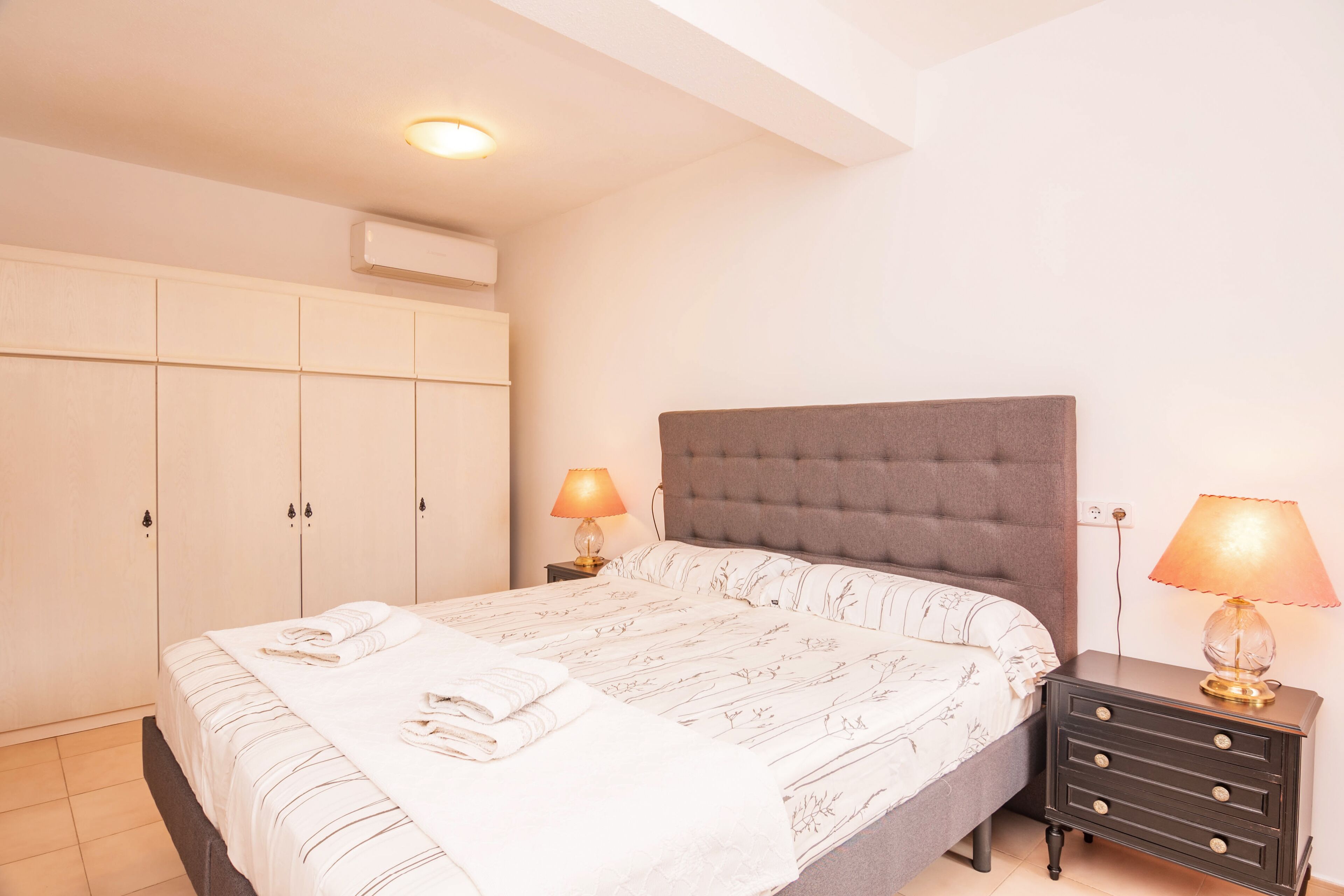 Een slaapkamer met een bed, nachtkastjes, een kledingkast en een plafondlamp.
