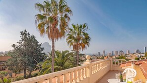 A balcony with a white railing, a table with chairs, and a view of a cityscape with palm trees. - Well maintained charming villa**** near the sea Lots of privacy, separate studio (Calp)