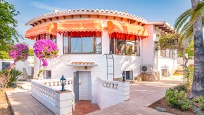 A white building with a curved roof and orange awnings, surrounded by a garden with pink flowers and a palm tree. - Well maintained charming villa**** near the sea Lots of privacy, separate studio (Calp)