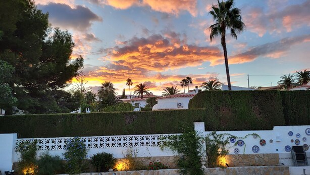 A pool area with a view of a sunset, palm trees, and a white building with decorative tiles. - Well maintained charming villa**** near the sea Lots of privacy, separate studio (Calp)