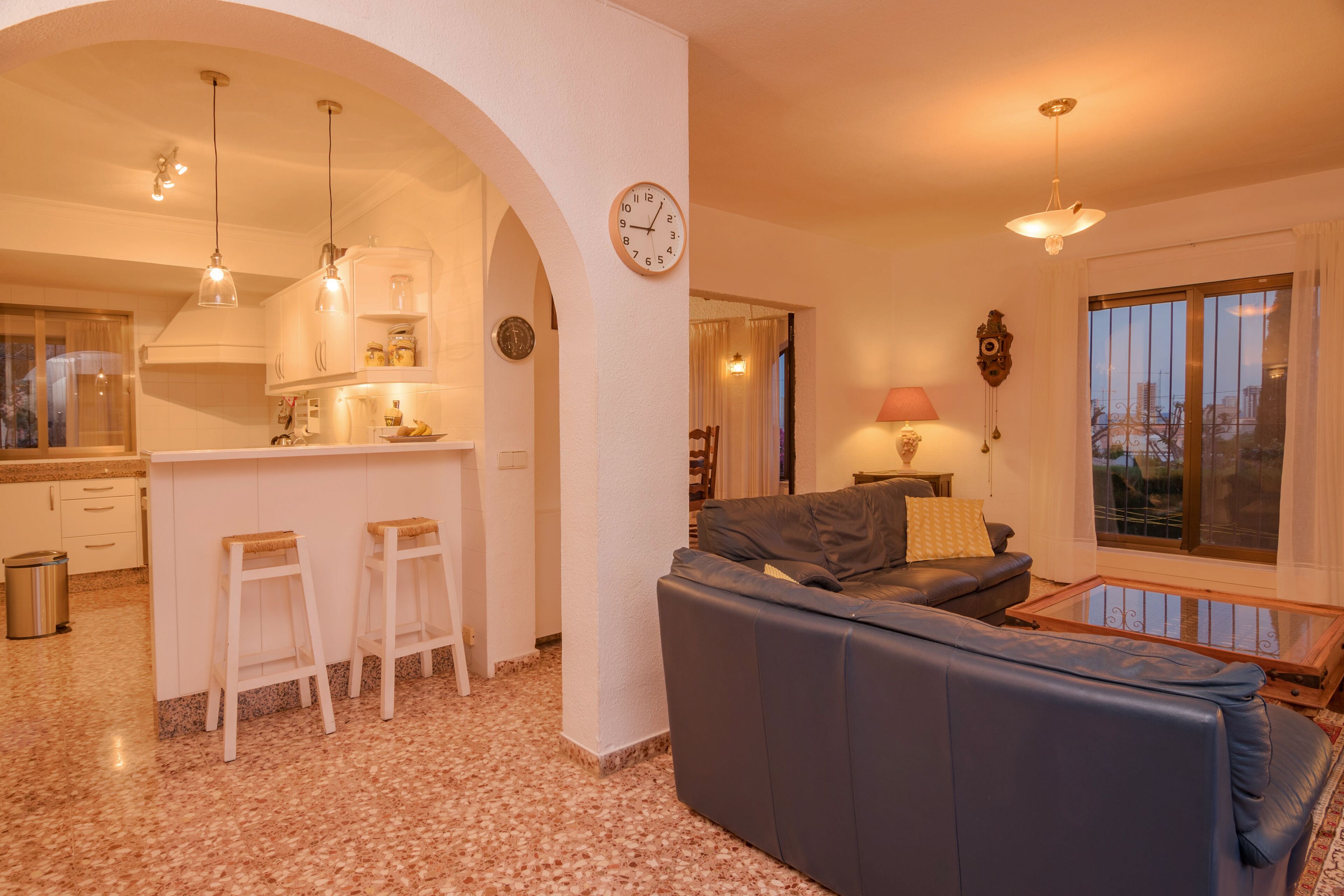 Un salon moderne avec un canapé et une table basse, une cuisine avec des meubles blancs et un coin repas comprenant une table et des chaises.