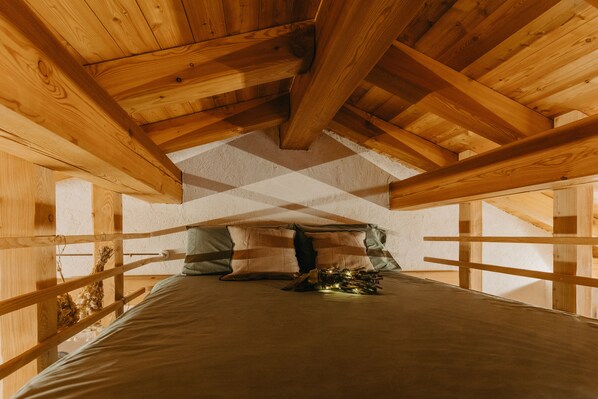 Techo de madera con diseño inclinado, una cama con almohadas y una pequeña mesa con un adorno.