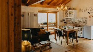 A cozy living room with a wooden ceiling, a dining area with a table and chairs, and a kitchen with a refrigerator and cabinets.