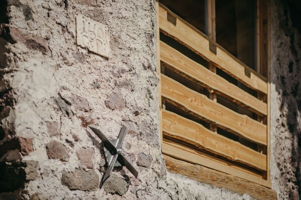 A rustic building exterior with a weathered stone wall and wooden window shutters.