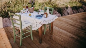 A wooden deck with a table set for a meal, featuring a lace tablecloth, a bowl of blueberries, and various jars and bottles.
