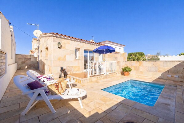 A poolside area with lounge chairs, a small table, and a blue umbrella.