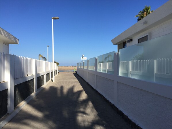 Un sendero bordeado por paredes blancas con paneles de vidrio que conduce a una playa.