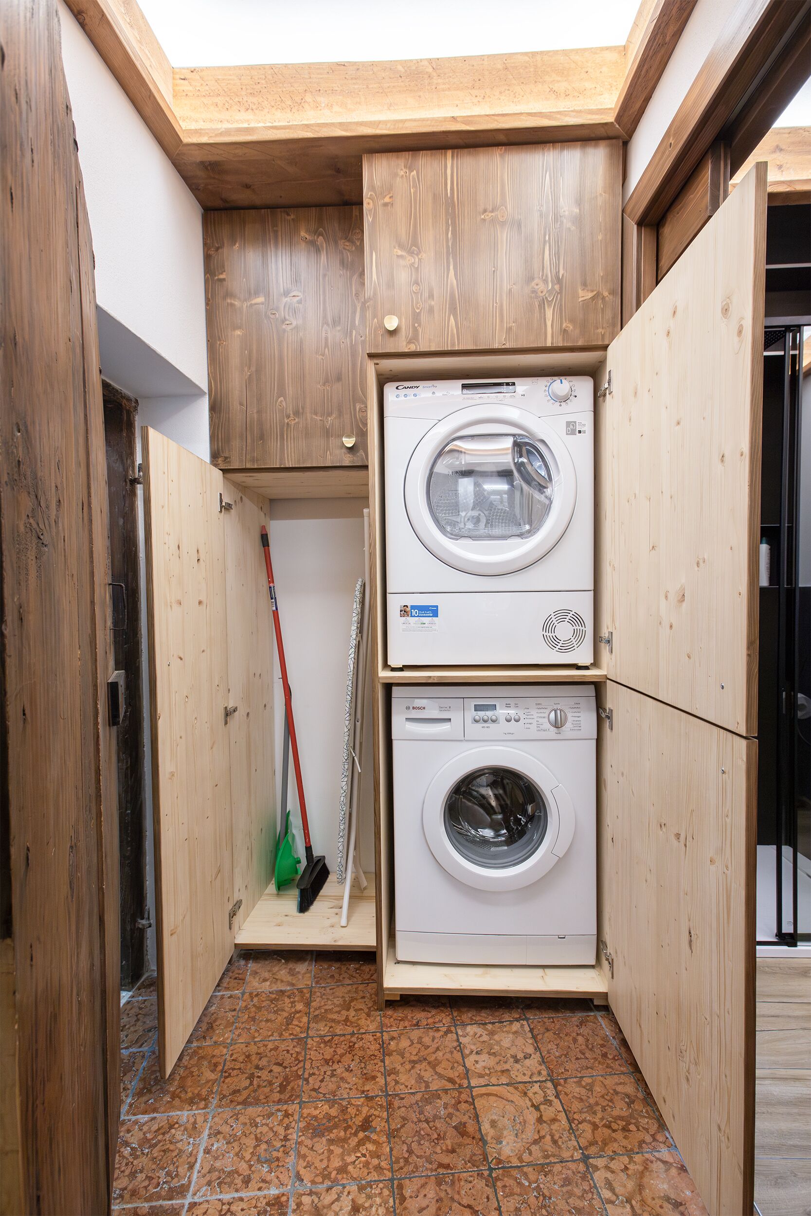 A laundry room with two stacked washing machines, a broom, and a mop.