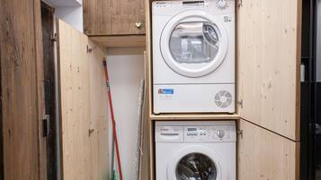 A laundry room with two stacked washing machines, a broom, and a mop.