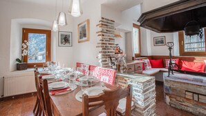 A dining area with a long wooden table set for a meal, a brick wall, and a window with a view. - Typical Cadore house, 15 minutes from Cortina, 4 big bedrooms and 3 bathrooms  (Vodo Di Cadore)