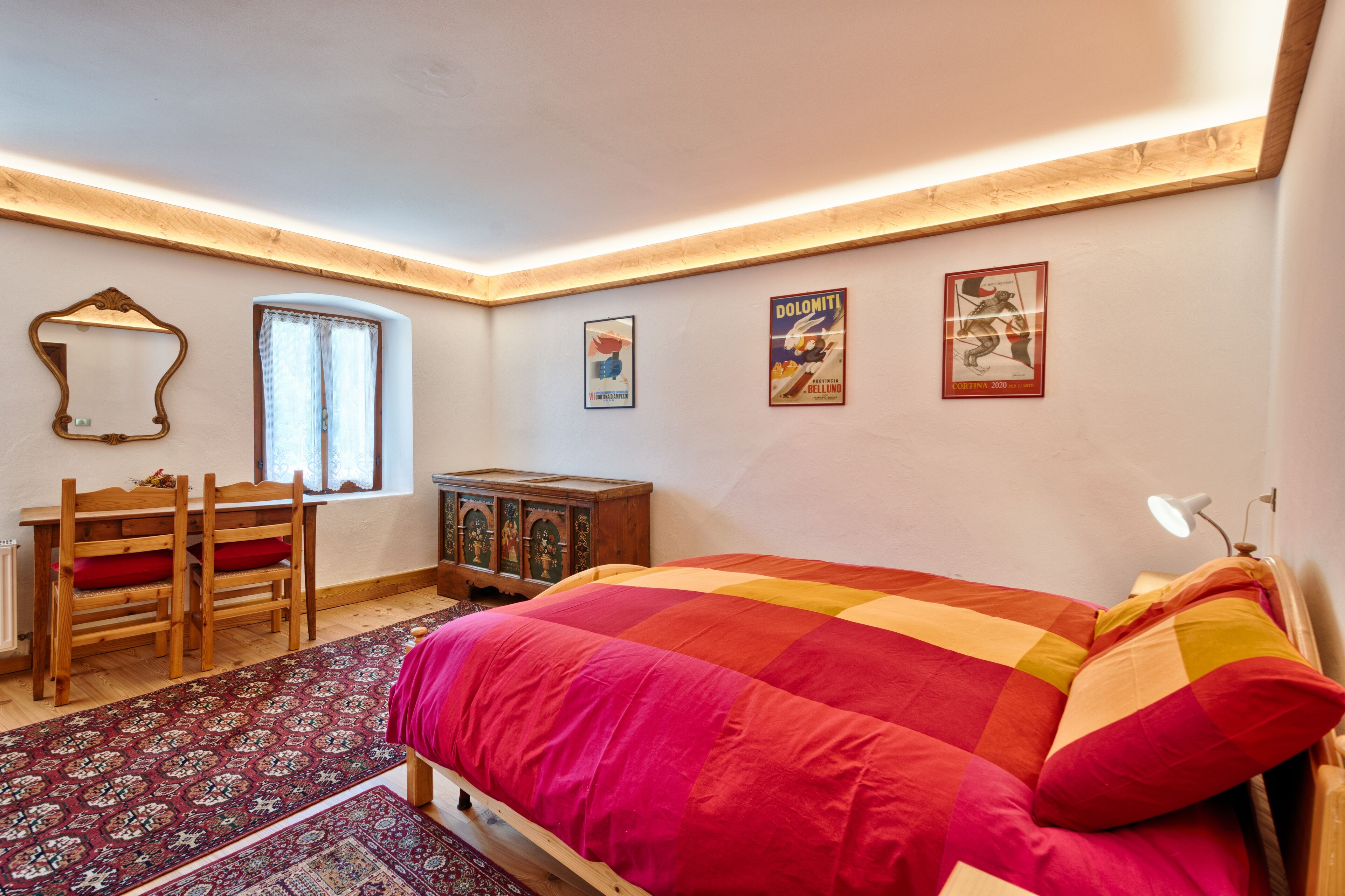 A bedroom with a large bed, a wooden desk, a chair, a cabinet, and a window.