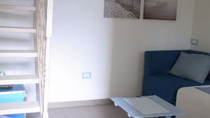 Une pièce avec un escalier, un canapé bleu, une petite table et quatre tableaux encadrés accrochés au mur.