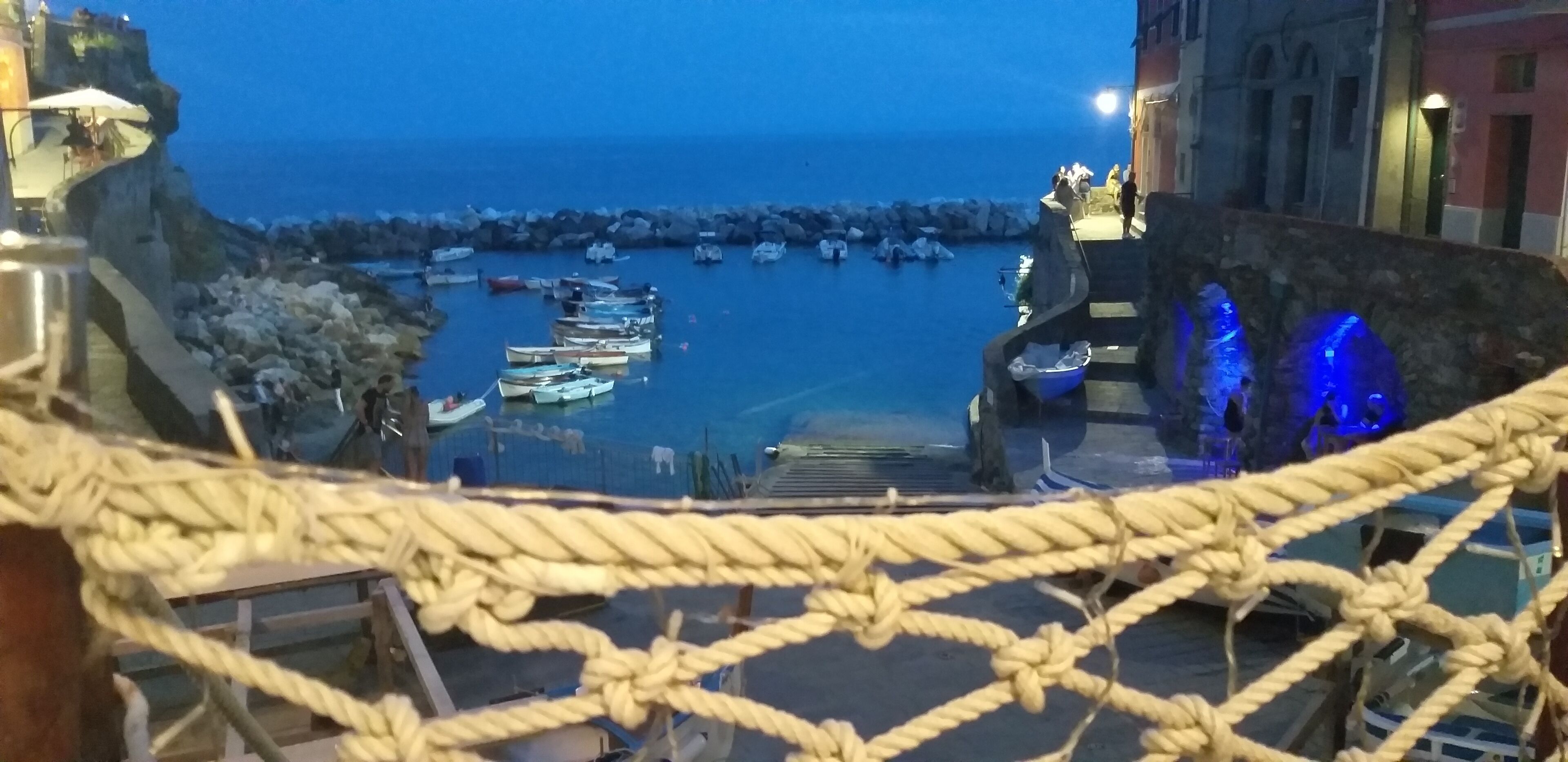 A rope bridge over a rocky area with boats docked in the water below.