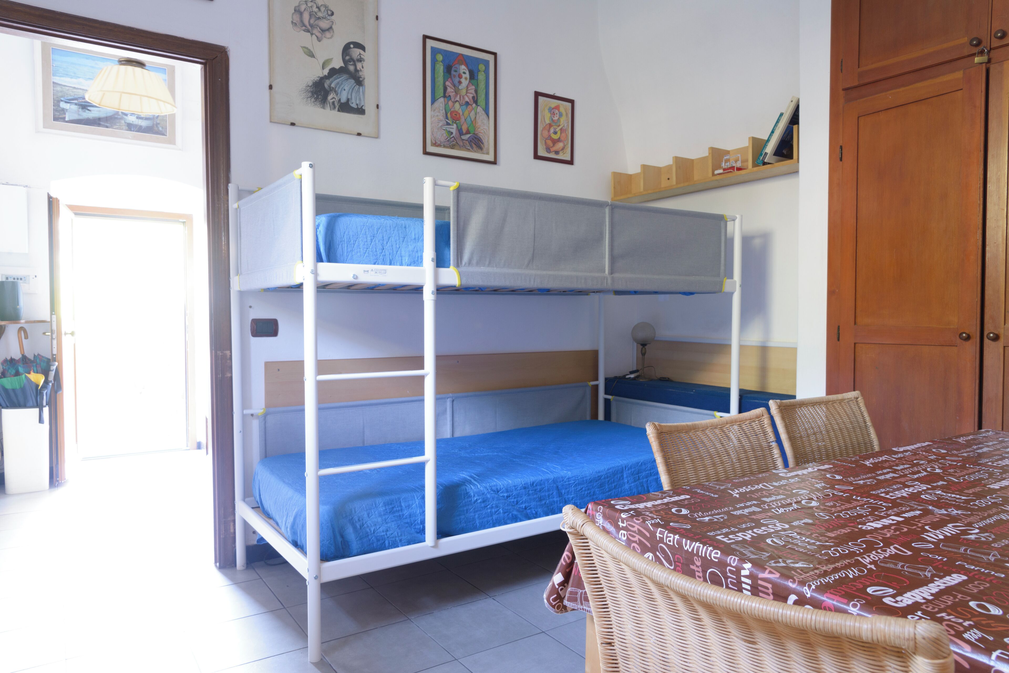 Una habitación con literas, una mesa de comedor, sillas de mimbre y un armario de madera.