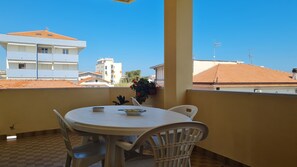 Un balcon avec une table ronde et des chaises, un pot de fleurs et une vue sur des bâtiments aux toits recouverts de tuiles orange.