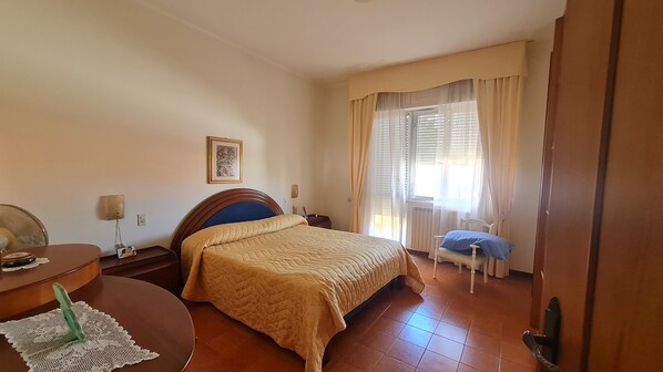 Un dormitorio con cama, mesita de noche, silla y ventana con cortinas.