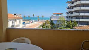 Un balcón con vista al mar, edificios y una mesa con sillas.