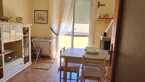 Una cocina con una mesa de comedor, sillas, una lámpara colgante y un ventanal con persianas.