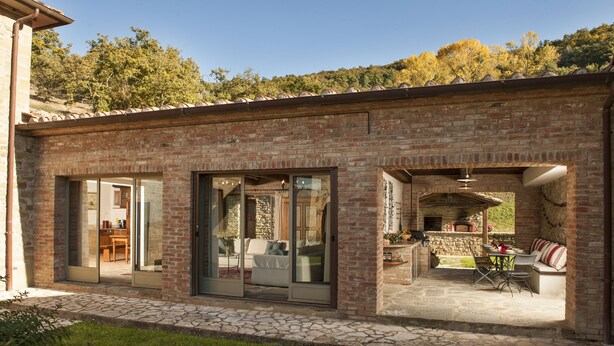 Una casa de ladrillo con un patio que incluye una mesa y sillas para comer, un sofá y una chimenea.