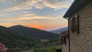 Un edificio de piedra con vista a un valle y colinas al atardecer.