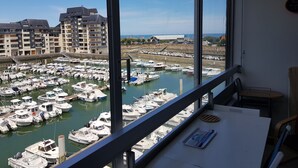 A view from a balcony overlooking a marina with numerous boats docked, a building with balconies in the background, and a clear sky. - La Marina, Normandy, Apartment 4 people with sea view and port (Courseulles-sur-Mer)