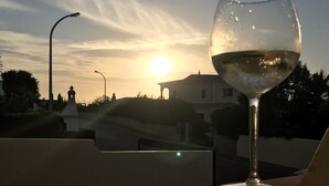 Ein Glas Weißwein auf einem Tisch mit Blick auf einen Sonnenuntergang und eine Gebäudesilhouette.
