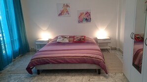 Un dormitorio con una cama, dos mesitas de noche y una mesilla auxiliar. Hay dos lámparas de pared a cada lado de la cama.