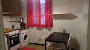 Cocina compacta con lavadora, microondas y una pequeña mesa con sillas.