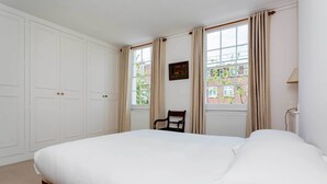 Une chambre avec un grand lit, une chaise et une fenêtre avec des rideaux.